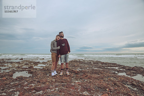 Junges schwules Paar  das Hand in Hand am Strand steht.