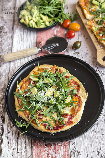 Vegetarische Pizza mit Avocado  Rucola  Tomaten und Parmesan auf dem Teller