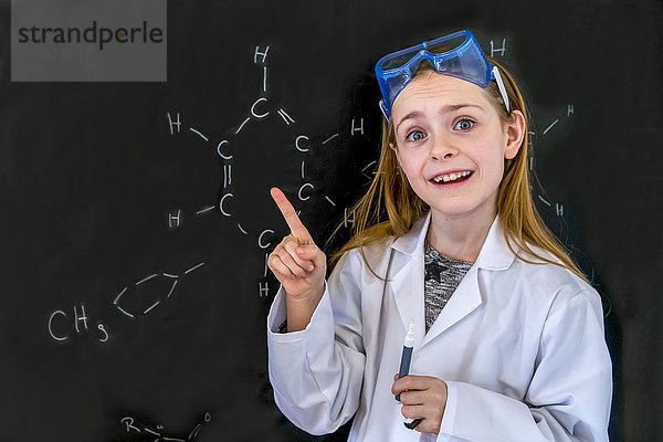 Porträt des Mädchens mit Arbeitsmantel und Schutzbrille vor der Tafel mit chemischen Formeln