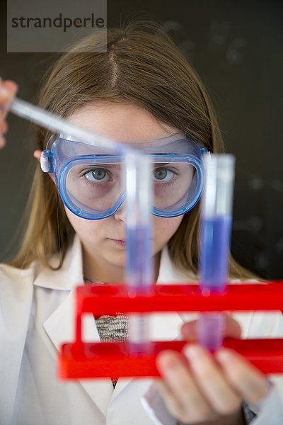 Porträt eines Mädchens mit Arbeitsmantel und Schutzbrille beim chemischen Experiment