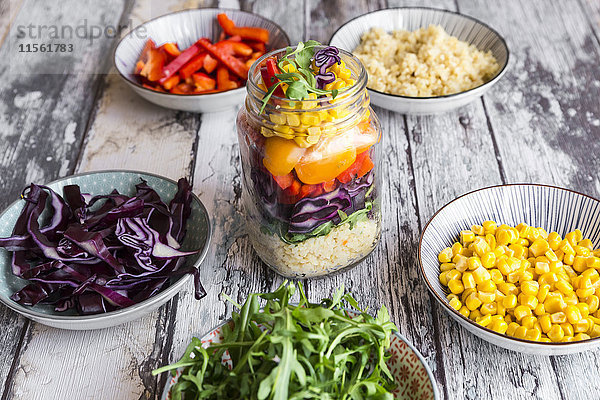 Glas Regenbogensalat mit Bulgur  Rucola und verschiedenen Gemüsen und Schalen mit Zutaten