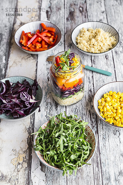 Glas Regenbogensalat mit Bulgur  Rucola und verschiedenen Gemüsen und Schalen mit Zutaten
