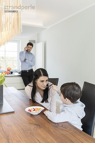 Mutter und Sohn beim Frühstück mit Vater am Telefon im Hintergrund