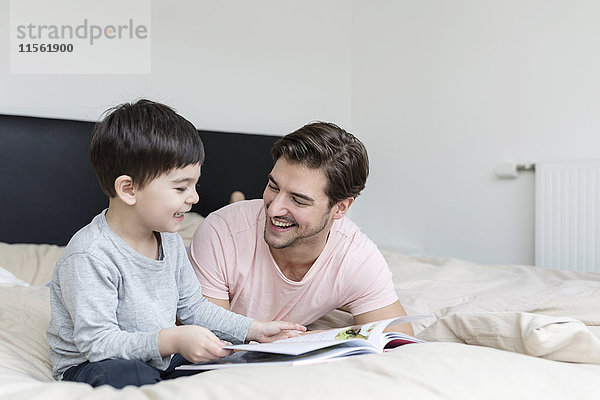 Glücklicher Vater und Sohn beim Lesen eines Buches im Bett