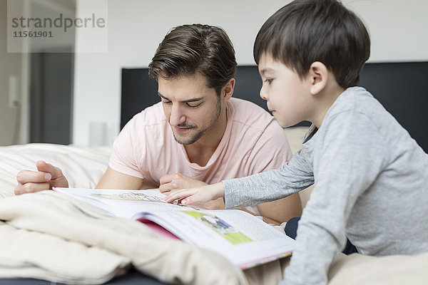 Vater und Sohn beim Lesen eines Buches im Bett