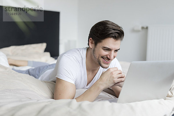 Lächelnder Mann auf dem Bett liegend mit Laptop
