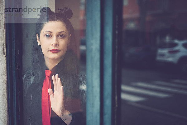 Porträt einer dunkelhaarigen jungen Frau mit roter Krawatte hinter einer Glastür stehend.