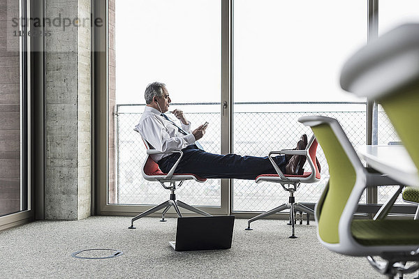 Senior Manager im Büro sitzend auf Stühlen mit erhobenen Füßen telefonierend