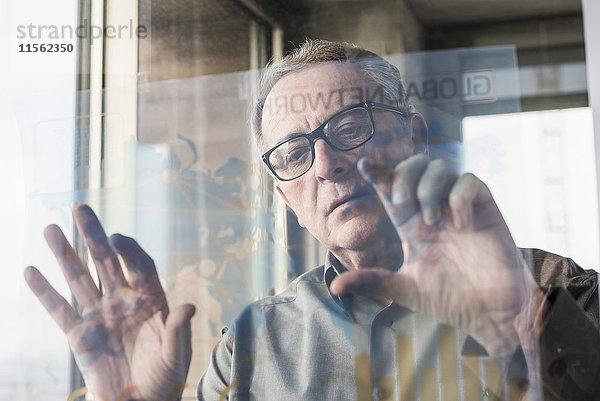 Senior Geschäftsmann berührt transparente Projektionswand im Büro