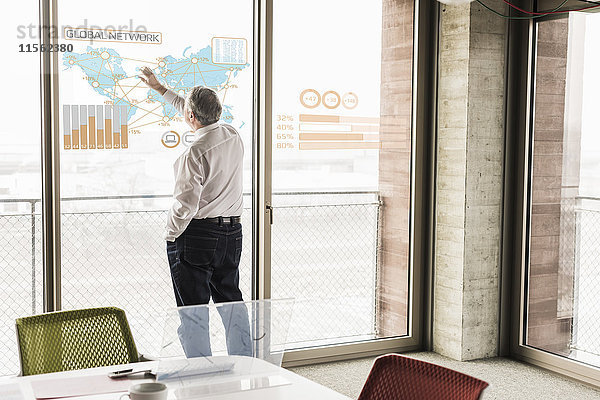 Geschäftsmann berührt Fensterscheibe mit Weltkarte und globalem Netzwerk im Büro