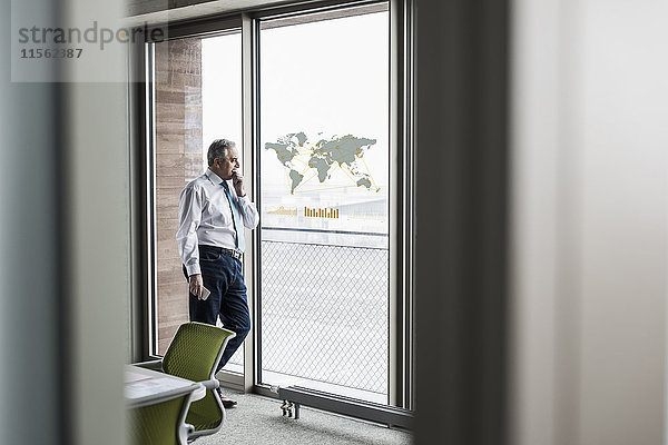 Geschäftsmann blickt auf Fensterscheibe mit Weltkarte im Büro