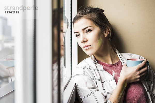 Junge Frau mit Kaffeetasse und Blick aus dem Fenster