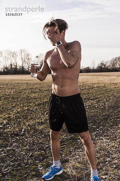 Barechested Athlet in der ländlichen Landschaft gießt Wasser über sein Gesicht