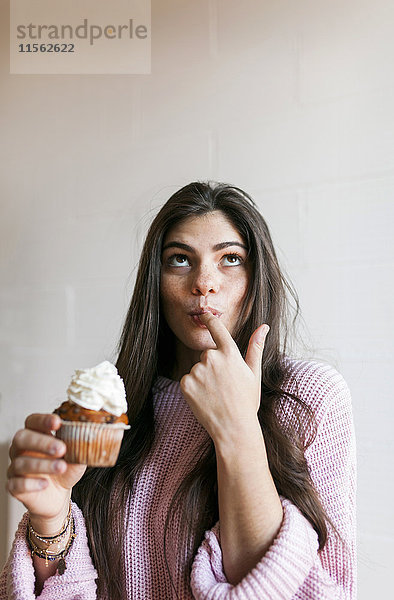 Junge Frau beim Essen einer Tasse Kuchen mit Schlagsahne  Finger lecken
