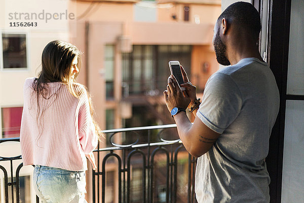 Junges Paar steht auf dem Balkon  macht Smartphone-Fotos