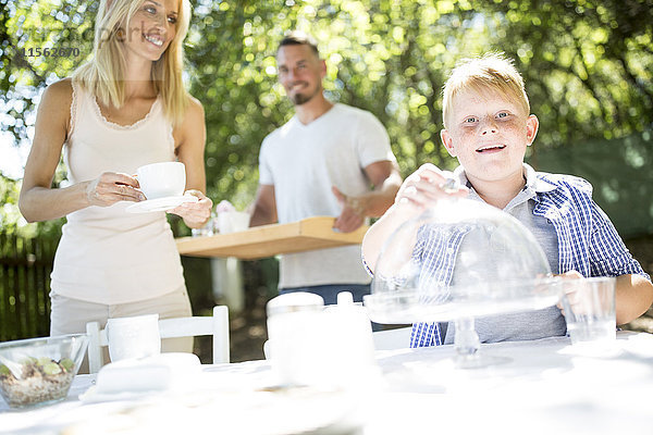Lächelnder Junge mit seinen Eltern beim Gartentischdecken