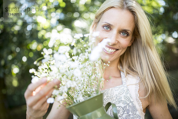 Lächelnde Frau hält Krug mit Blumen im Freien