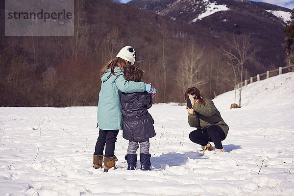 Mutter fotografiert zwei Kinder in der Winterlandschaft