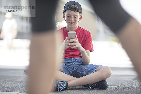 Junge mit Smartphone  sitzend auf Skateboard