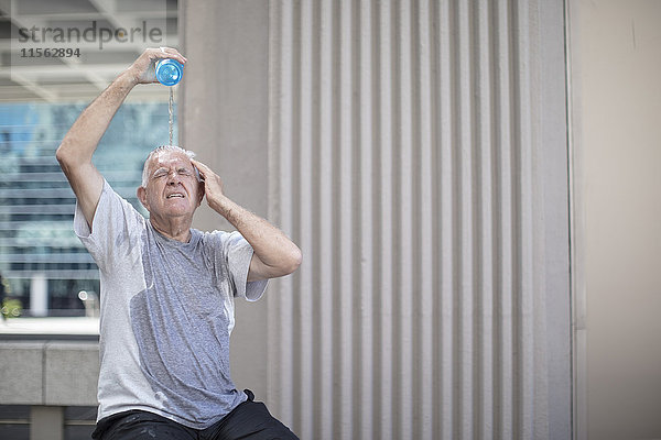 Seniorensportler macht eine Pause und gießt Wasser über den Kopf