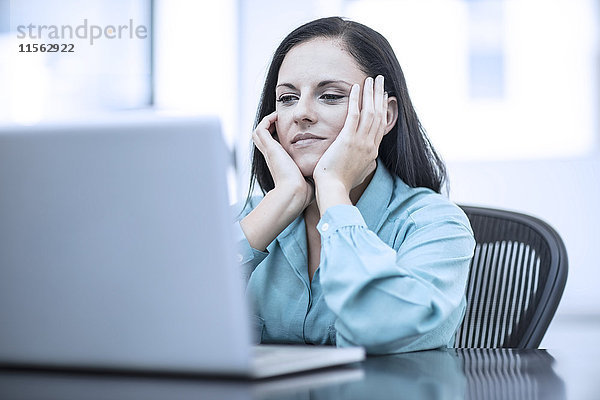 Frau mit dem Kopf in den Händen  die in einem Büro hinter dem Computer sitzt.