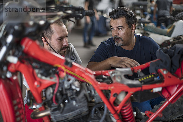 Zwei Mechaniker arbeiten zusammen an einem Motorrad in der Werkstatt.