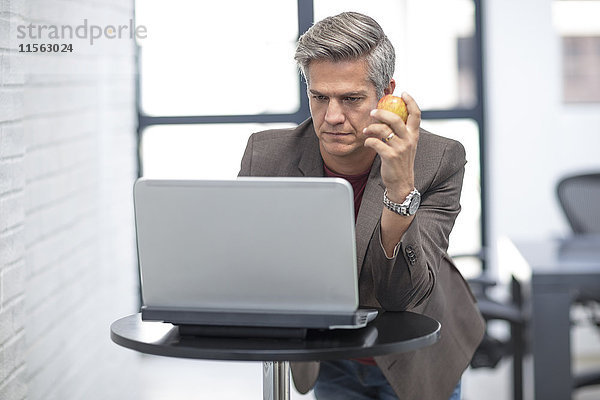 Geschäftsmann schaut auf Laptop  hält Apfel in der Hand