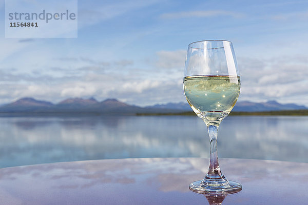 Ein mit Weißwein gefülltes Weinglas auf einer Tischfläche neben dem Tikchik Lake  Wood-Tikchik State Park  Südwest-Alaska  USA