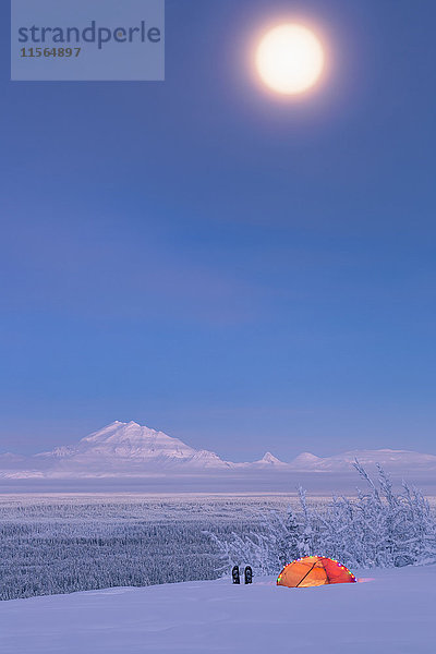 Der Vollmond über dem verschneiten Mount Drum und dem Copper River Valley mit einem Zelt und Schneeschuhen im Vordergrund  Southcentral Alaska  USA  Winter