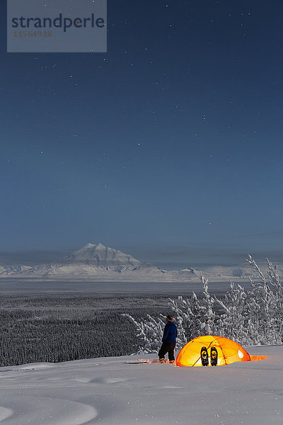 Mann betrachtet Mount Drum und das Copper River Valley mit einem Zelt und Schneeschuhen im Vordergrund  Süd-Zentral-Alaska  USA  Winter