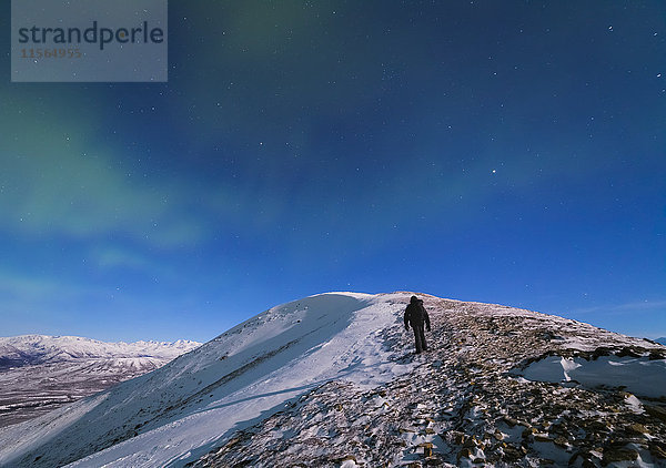 Ein Mann klettert in einer Mondnacht bei Minusgraden auf den Gipfel des Donnelly Dome (in der Nähe von Delta Junction)  um das Polarlicht zu fotografieren.