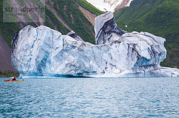 Ein Seekajaker wird von einem riesigen Eisberg in der Bear Glacier Lagoon im Kenai Fjords National Park in den Schatten gestellt.