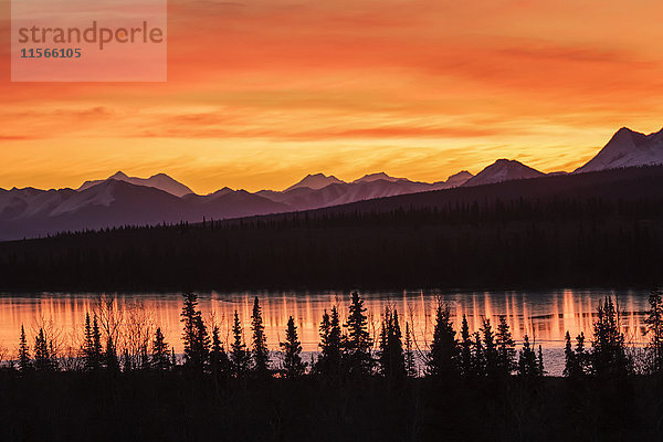 Glühende Wolken bei Sonnenaufgang über einer Bergkette und einem See  Alaska im Frühherbst; Cantwell  Alaska  Vereinigte Staaten von Amerika'.