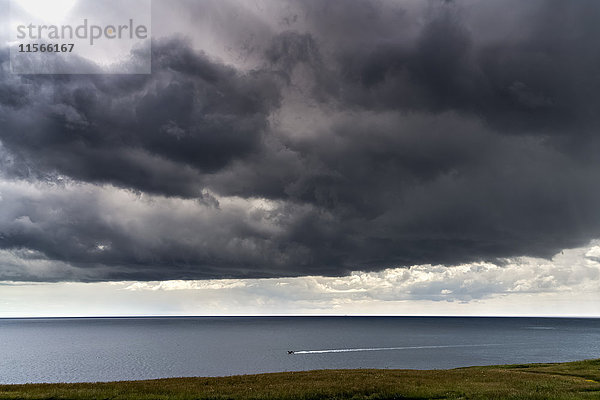 Bedrohliche dunkle Wolken über dem Meer und ein kleines Boot  das die Küste entlang fährt; South Shields  Tyne and Wear  England'.