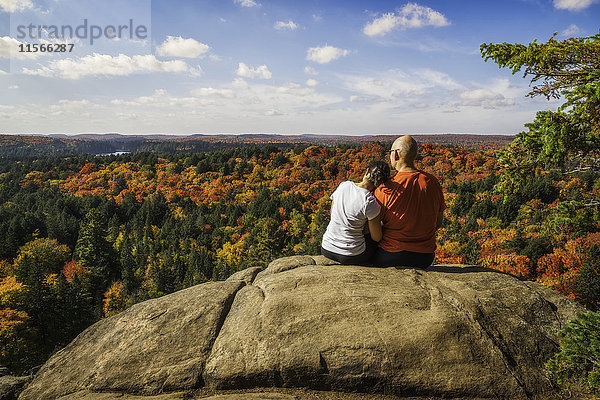 Paar sitzt auf einer Klippe mit Blick auf die Herbstfarben im Algonquin Park  die Frau hat den Kopf auf der Schulter des Mannes; Ontario  Kanada'.