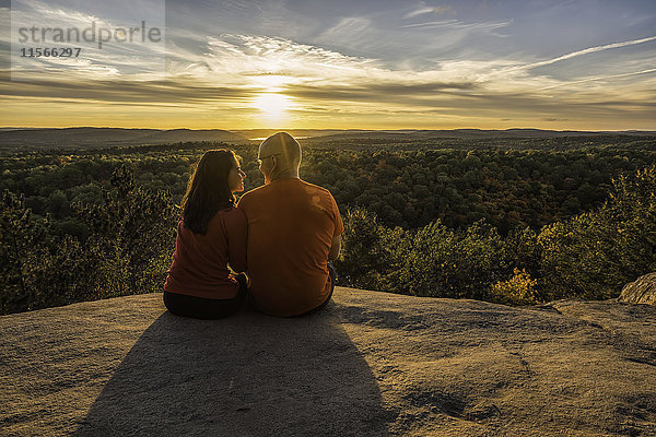 Paar sitzt auf einer Klippe mit Blick auf die Herbstfarben im Algonquin Park bei Sonnenuntergang; Ontario  Kanada'.