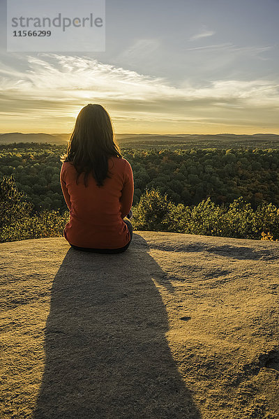 Frau sitzt auf einer Klippe mit Blick auf den Algonquin Park im Herbst bei Sonnenuntergang; Ontario  Kanada'.