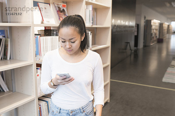 Junge Frau benutzt Mobiltelefon in der Bibliothek