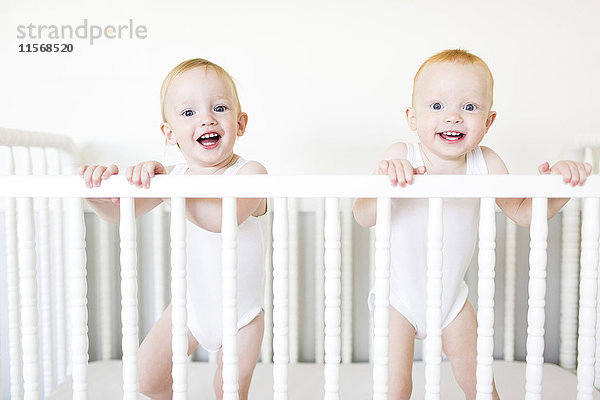 Zwillingsbrüder (12-17 Monate) in der Krippe stehend