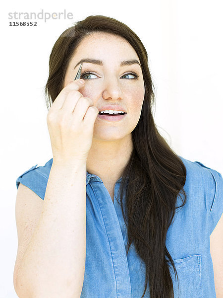 Frau mit blauem Oberteil zupft Augenbraue