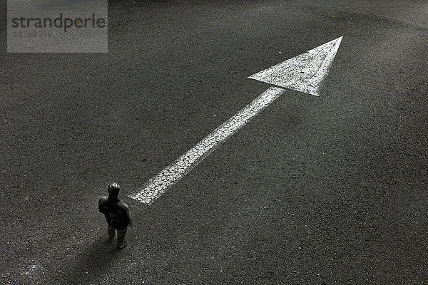 Mann schaut auf gezeichneten Pfeil auf der Straße  der die Richtung anzeigt