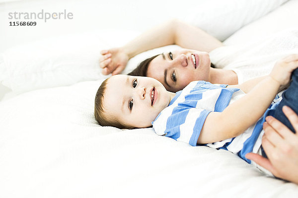Mutter liegt mit Sohn (4-5) auf dem Bett und lächelt