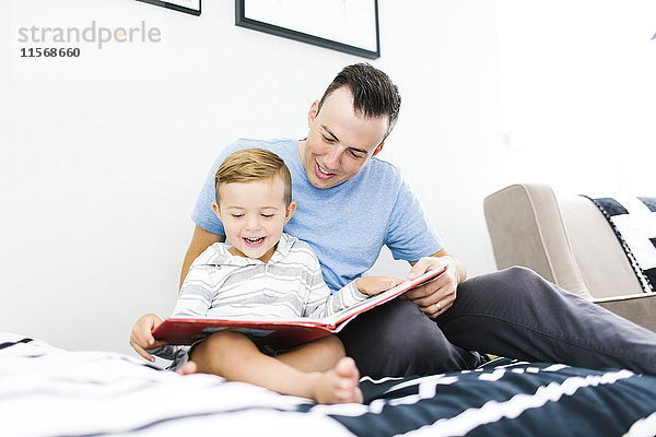Vater und Sohn (4-5) sitzen auf dem Bett und lesen ein Buch