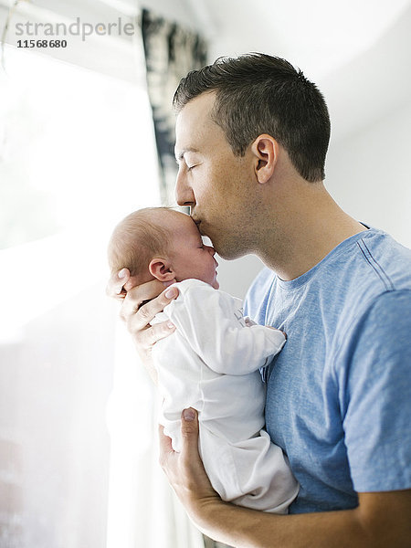 Vater trägt Tochter (0-1 Monate) und küsst sie
