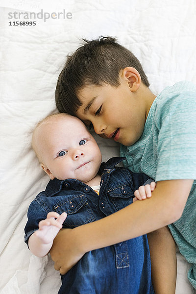 Zwei Brüder (6-11 Monate) liegen auf dem Bett und umarmen sich