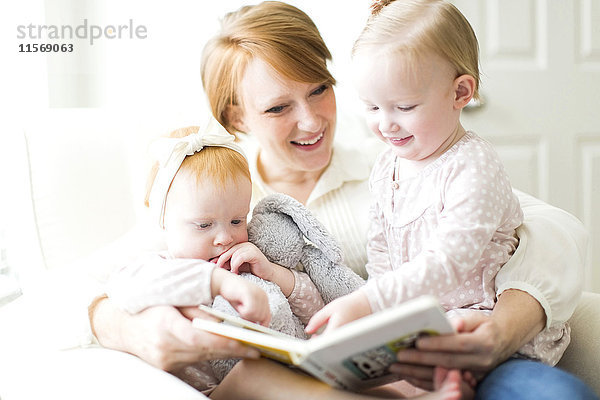 Mutter liest ihren Töchtern ein Buch vor ( 12-17 Monate )