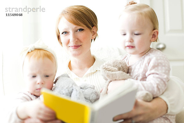 Porträt einer Mutter  die ihren Töchtern ein Buch vorliest (12-17 Monate)