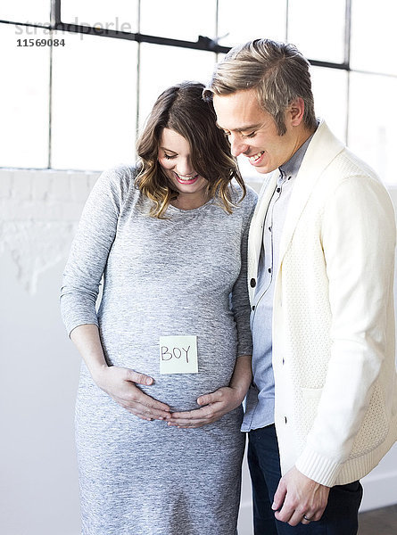 Porträt eines Mannes und einer lächelnden schwangeren Frau mit Haftnotiz auf dem Bauch