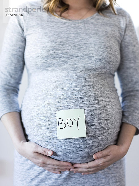 Porträt einer lächelnden schwangeren Frau mit Haftnotiz auf dem Bauch