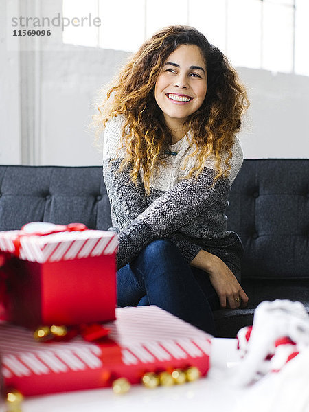 Glückliche Frau auf Sofa mit Weihnachtsgeschenken im Vordergrund